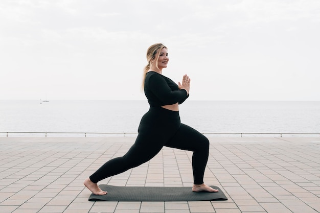 Plus size girl practicing yoga in front of the ocean on a summer day