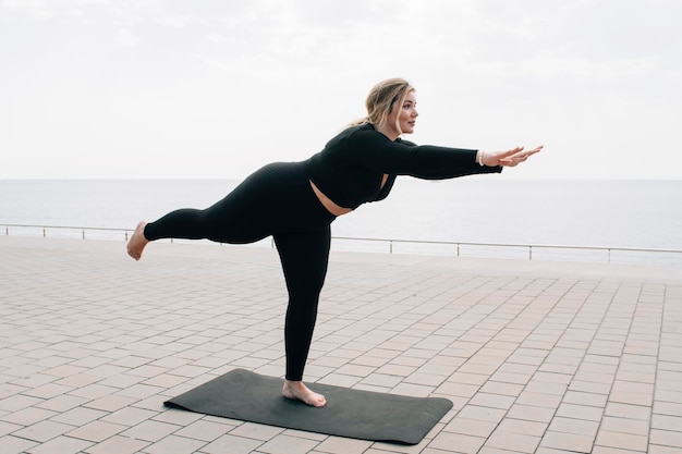 Plus size girl practicing yoga in front of the ocean on a summer day