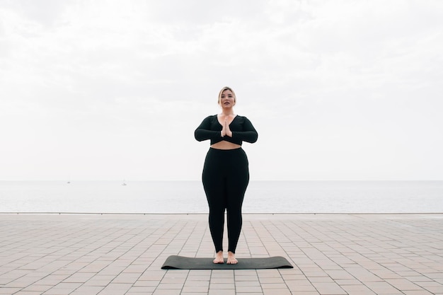 Plus size girl practicing yoga in front of the ocean