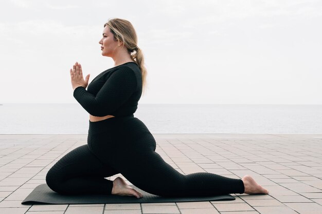 Plus size meisje dat yoga beoefent voor de oceaan op een zomerdag