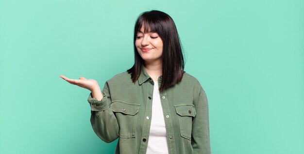 プラスサイズのきれいな女性は、幸せでさりげなく笑顔を感じ、側面の手に持っているオブジェクトやコンセプトを見て