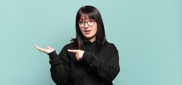 Plus size pretty woman smiling cheerfully and pointing to copy space on palm on the side, showing or advertising an object