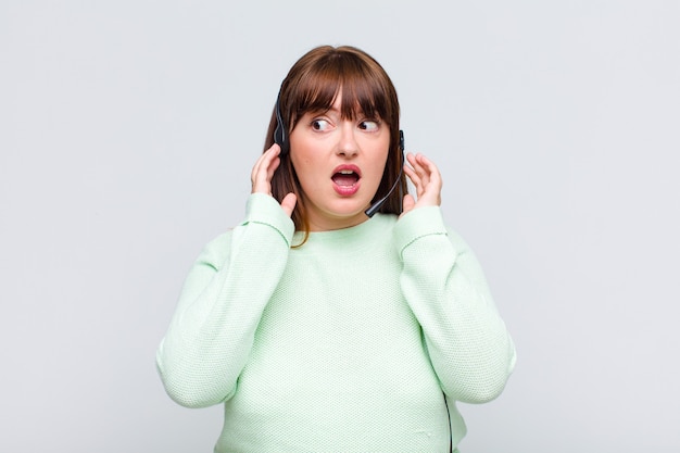 Plus size woman feeling happy, excited and surprised, looking to the side with both hands on face