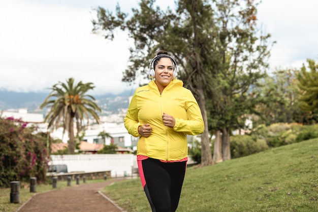 Plus size donna fare jogging all'aperto al parco cittadino - obiettivo principale sulle cuffie