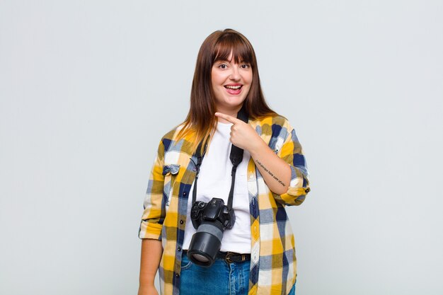 Plus size woman looking excited and surprised pointing to the side and upwards to copy space