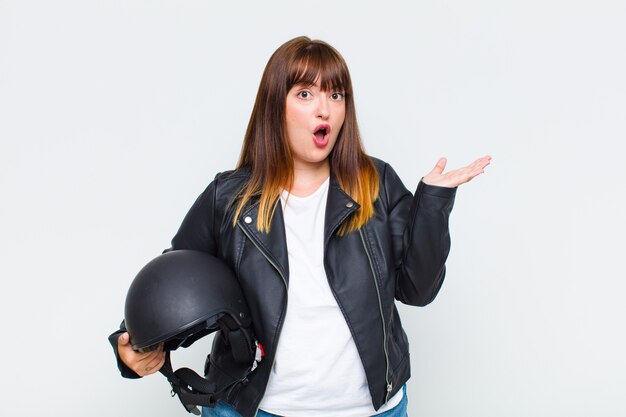 Plus size woman looking surprised and shocked, with jaw dropped holding an object with an open hand on the side