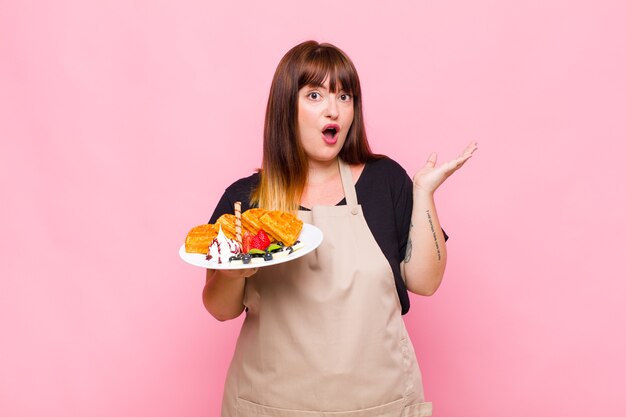 Plus size woman looking surprised and shocked, with jaw dropped holding an object with an open hand on the side