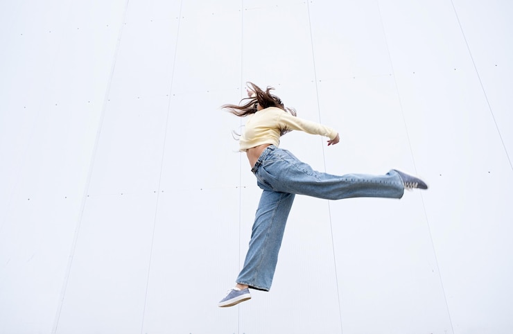 Photo 通りの白い壁の背景で踊っているカジュアルな服を着たサイズの女性