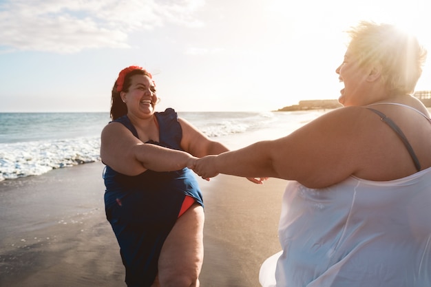 Taglie forti donne che ballano sulla spiaggia divertendosi durante le vacanze estive - donna formosa che ride insieme - corpo in sovrappeso e concetto di felicità - concentrarsi sul viso di donna giusta