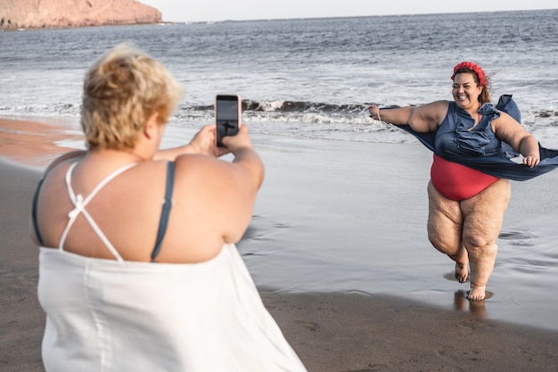 Photo plus size women friends having fun taking photos on the beach