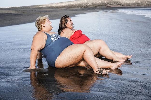 Plus size donne sedute sulla spiaggia che si divertono durante le vacanze estive