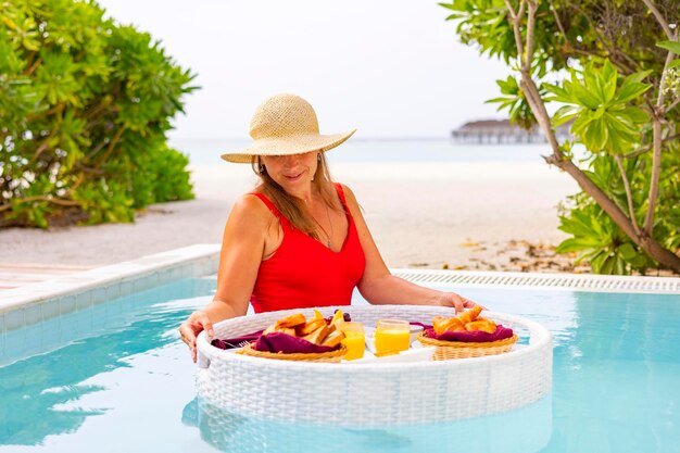 plus size young woman with served floating tray in swimming pool with drinks and snacks on tropical island resort in Maldives cocktails and canapes for romantic date in luxury hotel travel concept