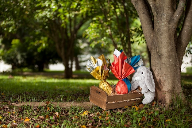 A plush rabbit holding a basket of brazilian Easters eggs under a tree