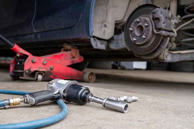 Pneumatic wrench tool on the asphalt and a car jack for lift up\
the body and changing the tire.