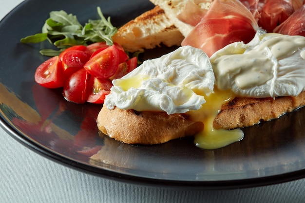 Poached egg on a piece of bread with salad, becon and tomato on the table