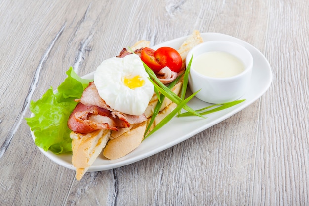 Photo poached egg with bacon cherry tomatoes onion on a baguette and white sauce