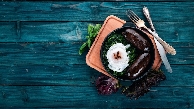 Poached egg with spinach and buckwheat sausage. On a wooden background. Top view. Copy space.