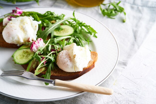 poached eggs with herbs, avocado and cucumber served on a plate on a light background