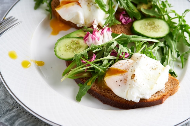 Poached eggs with herbs, avocado and cucumber served on a plate on a light background