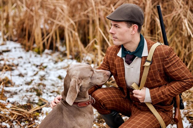 Poacher with gun and weimaraner dog breed friend in nature, sit together. autumn season