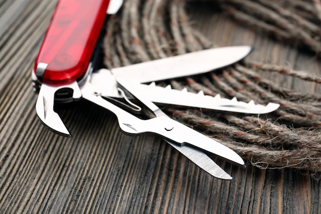 Pocket knife with rope on wooden table close up