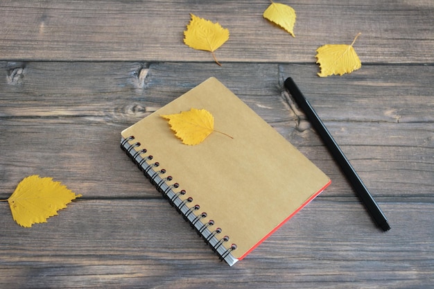 pocket notepad on the wooden background with pencil and dry autumn leaves