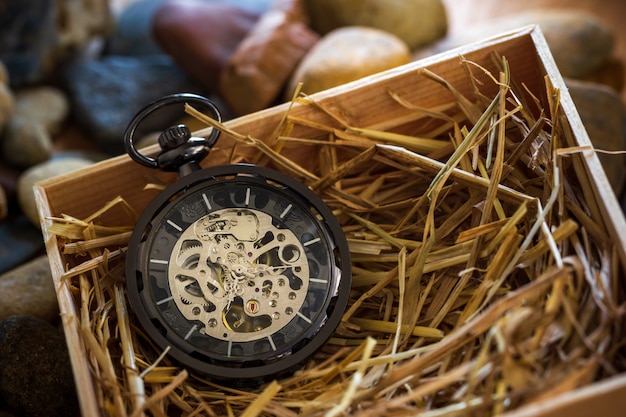 Foto avvolgitore per orologio da tasca su paglia di grano naturale in una scatola di legno.