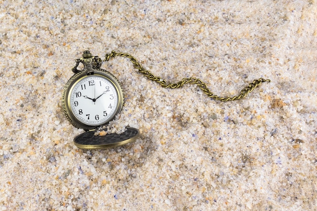 Pocket watch with chain in the sand. Time passing symbol.