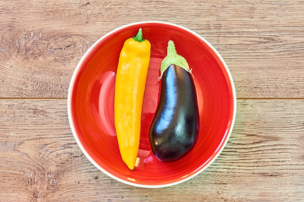 pod of yellow pepper and almost black eggplant on a red plate on a wooden tabletop