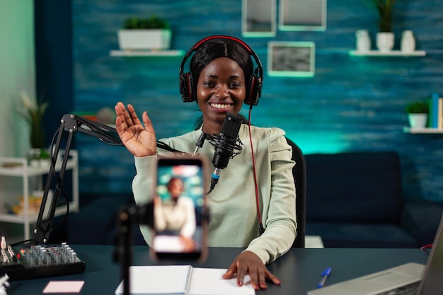 Podcast creator sitting at desk in vlogging studio greeting subscribers while recording video content for youtube channel. Social media influencer filming vlog talking into production micophone