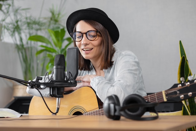 Podcast muziek audio content creatie mooie Europese vrouw podcaster in een hoed met een gitaar of guitar