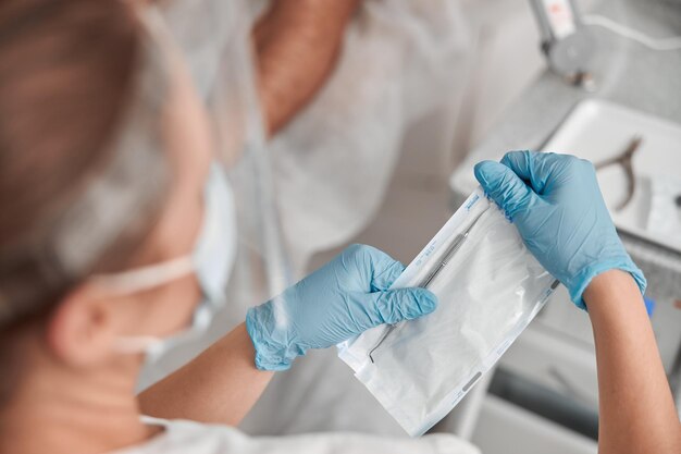 足病医は、クライアントの足の爪を美しく動かすために、滅菌金属プローブでパックを開きます