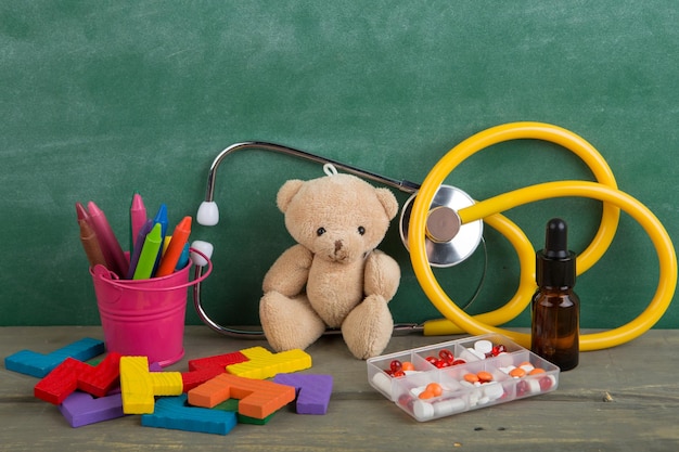 足病医の職場のおもちゃのクマ聴診器と木製の机の上の薬子供のヘルスケアの概念