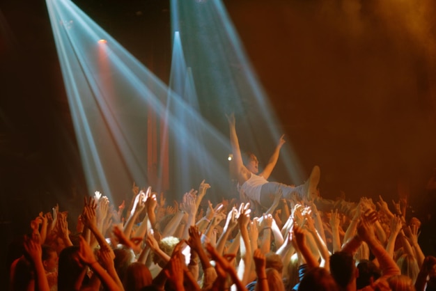 Foto podiumduikhanden en mensen op muziekfestival neonspot en energie tijdens live concertevenement dansplezier en groep opgewonden fans in arena bij rockshow optredens publiek met crowdsurfer
