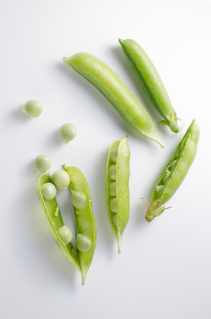 Pods of green peas on a white surface