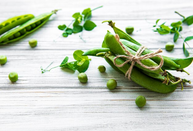 Baccelli di piselli con foglie di pisello su un fondo di legno bianco. cibo organico.