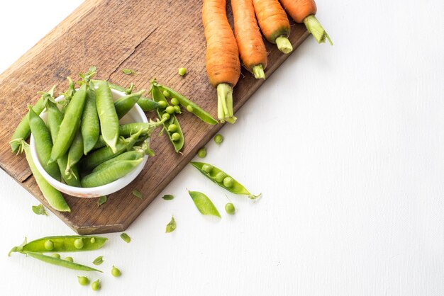 A pods of pea and carrot on wooden board