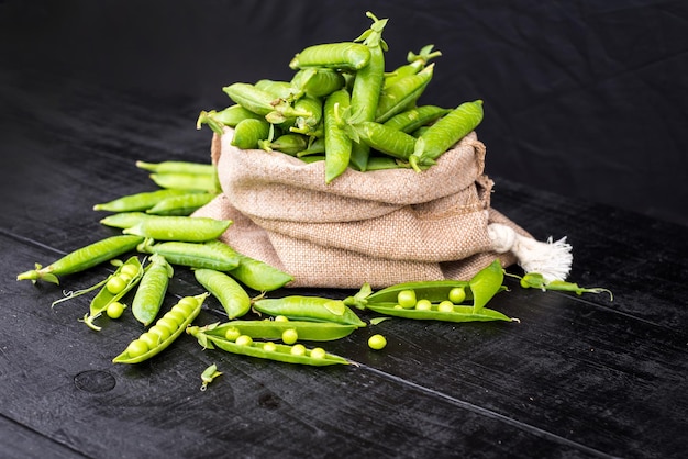 A pods of peas in a bag on black wooden background