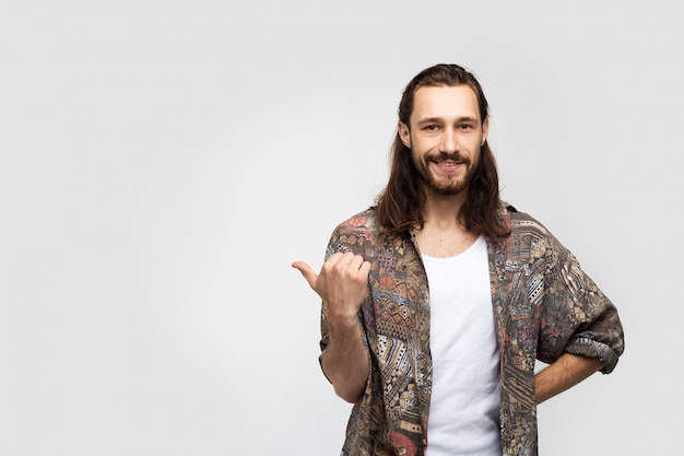 Point finger to side to place text, logo or advertisement. Hipster traveler stylish carefree man on a white studio background, people lifestyle