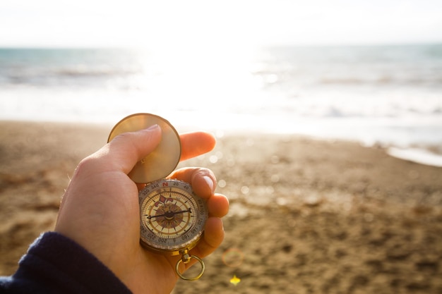Point of view photo of man holding compass in the hand on the sea and beach background