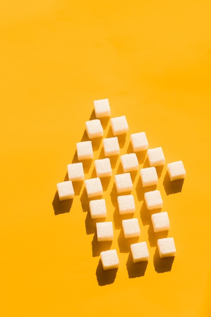 Pointer of white sugar cubes on yellow background