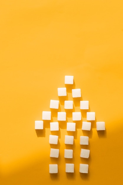 Pointer of white sugar cubes on yellow background