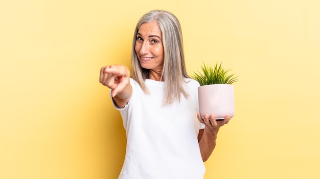 Pointing at camera with a satisfied, confident, friendly smile, choosing you holding a decorative plant