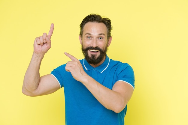 Pointing direction. Man pointing index fingers yellow background. Guy beard and mustache shows direction. Look at that advertisement. Man bearded cheerful fresh idea. Check it out.