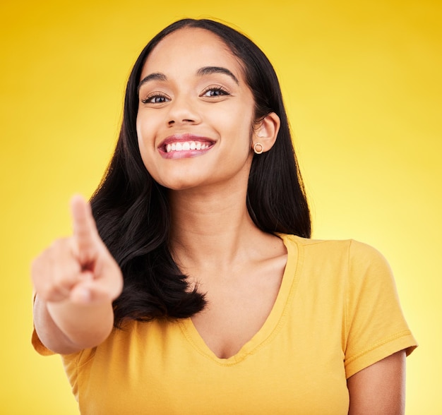 Pointing happy and portrait of a woman in a studio with a smile and positive face expression Happiness finger and female model from Puerto Rico with a showing hand gesture by a yellow background