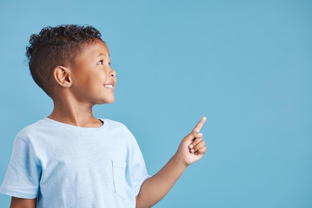 pointing space and show with boy in studio for idea announcement and information direction notification and decision with child on blue background for promotion presentation and process mockup