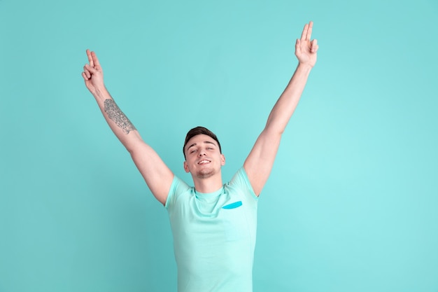 Pointing, winning. Caucasian young man's portrait isolated on blue studio wall