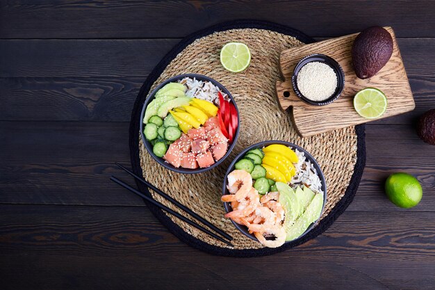 Foto poke-bak met zalm, garnalen, avocado, rijst, komkommer, mango, peper en sesamzaad op donkere houten achtergrond