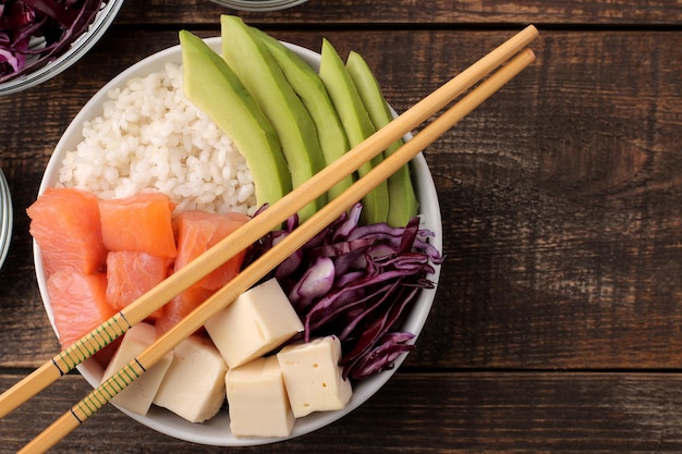 Poke bowl Hawaiiaans voedselbord van rijst, zalm, avocado, kool en kaas op een bruin houten tafelblad