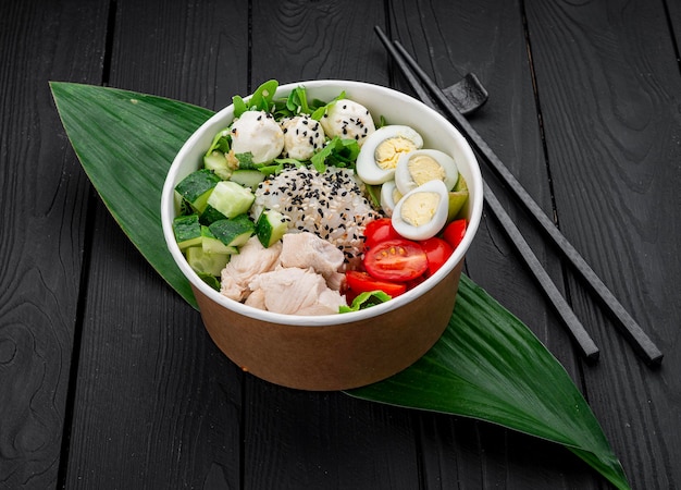 Poke bowl met kip, rijst, avocado, komkommer, roomkaas, tomaat en kwarteleitje op donkere achtergrond